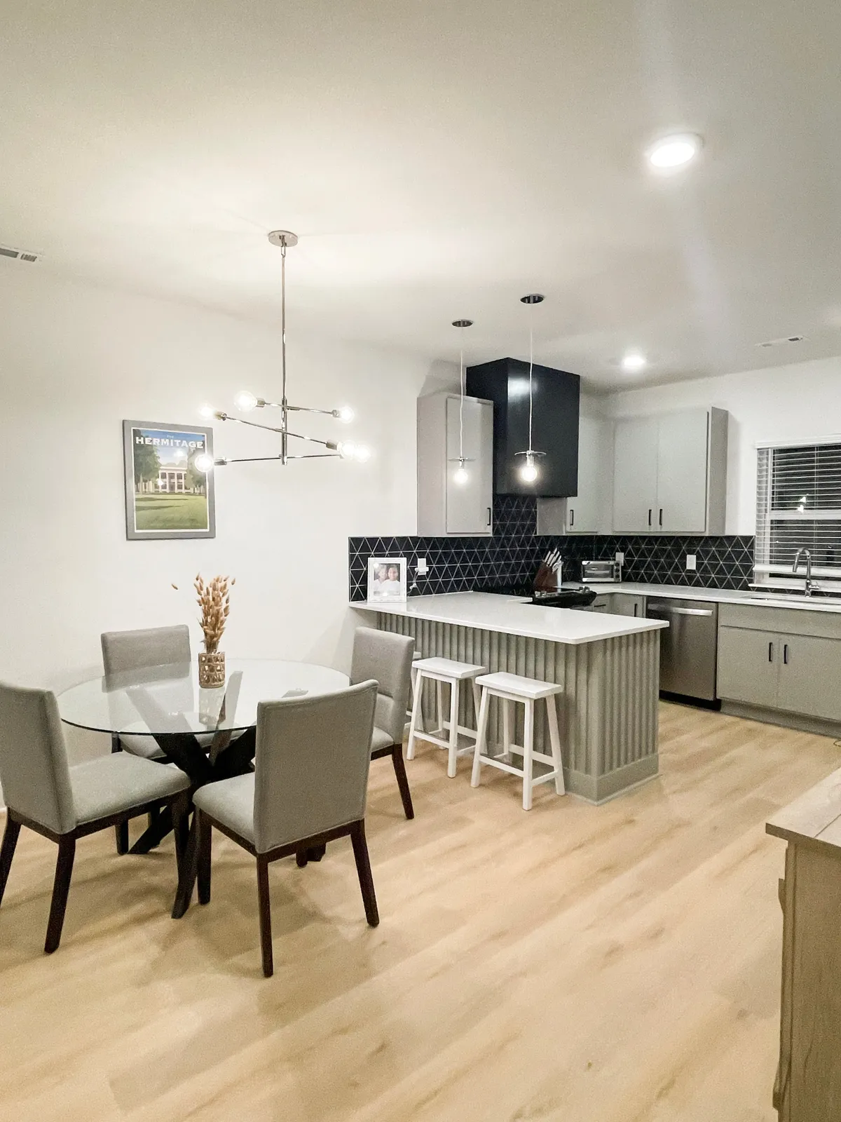 A cozy dining area adjoins the kitchen, featuring a handsome dining table, stylish pendant lights, and a bold black backsplash. The scene hints at comfortable, intimate meals and lively gatherings.