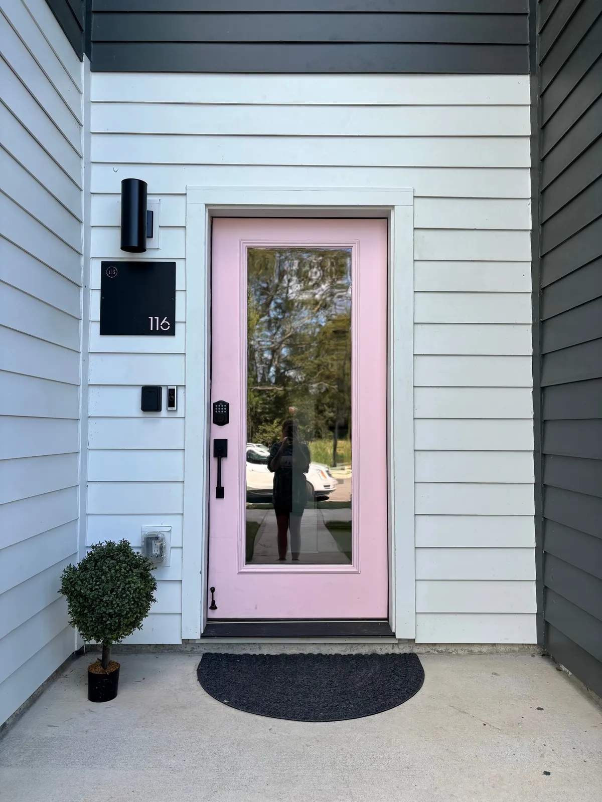 A friendly exterior entry featuring a vibrant pink door, bold black house numbers, and a small shrub, emphasizing a welcoming atmosphere. The scene captures the moment of arriving at or leaving from the home, reinforcing the idea of stress-free comings and goings.