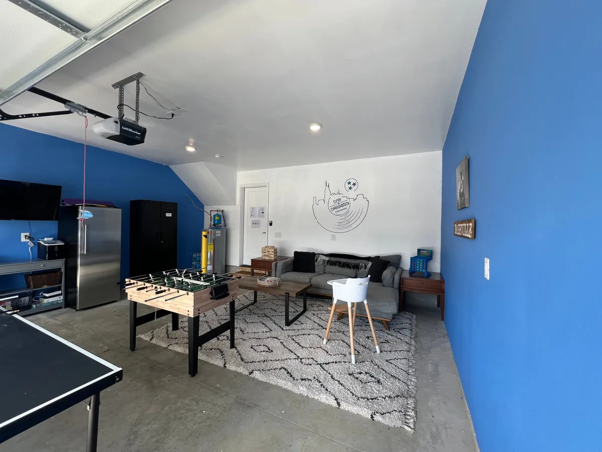 A playful garage game room featuring a foosball table, a comfortable sofa, and a striking blue accent wall. The space is designed for fun and friendly competition, offering a relaxed setting for game nights or casual group gatherings.