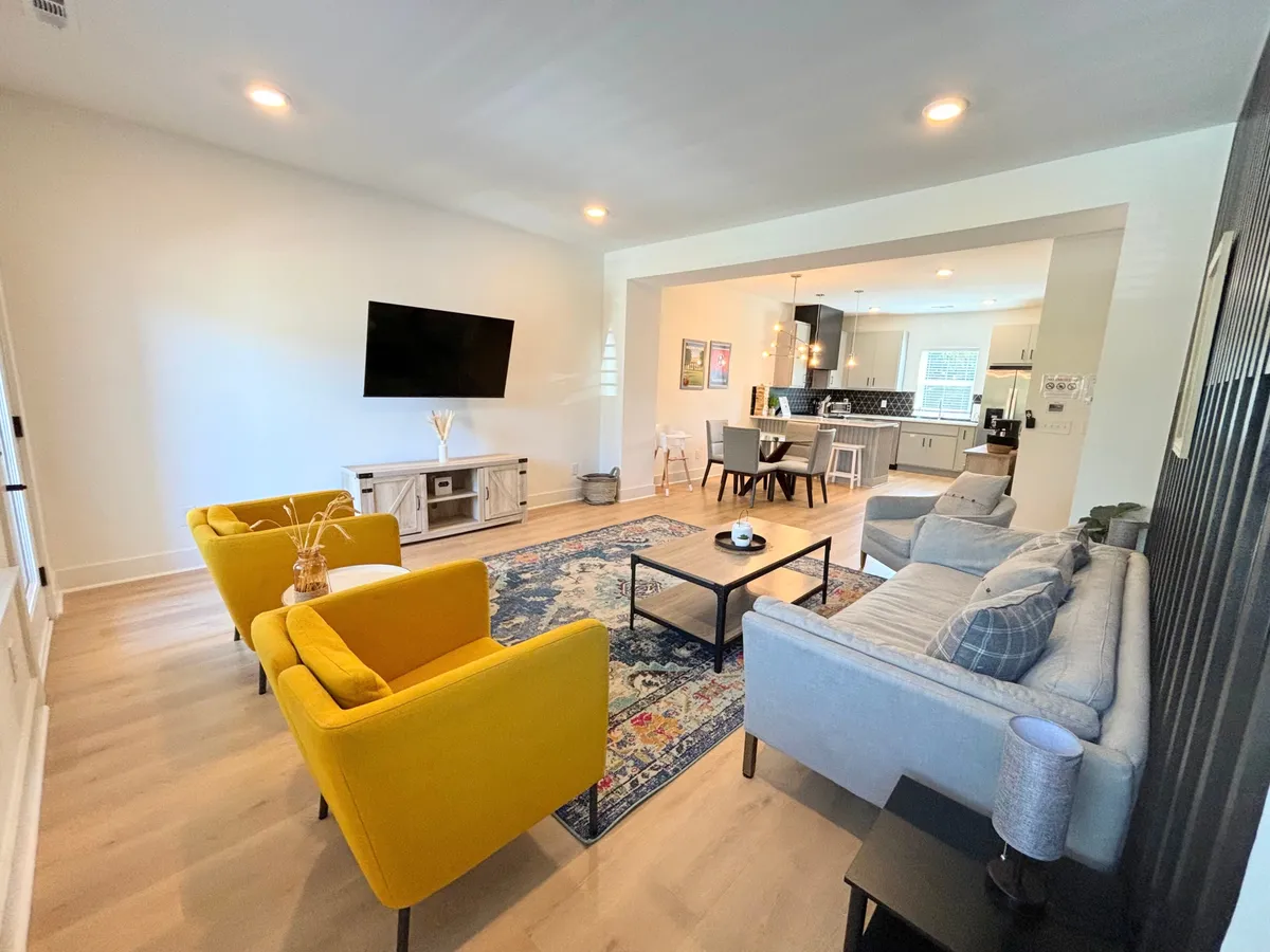 A cozy living room area with yellow armchairs, a gray sofa, a coffee table, and a large TV mounted on the wall. The space is decorated in a modern style, inviting guests to relax, socialize, and enjoy entertainment together. The layout is open and bright, perfectly suited for group gatherings, movie nights, or celebrations.
