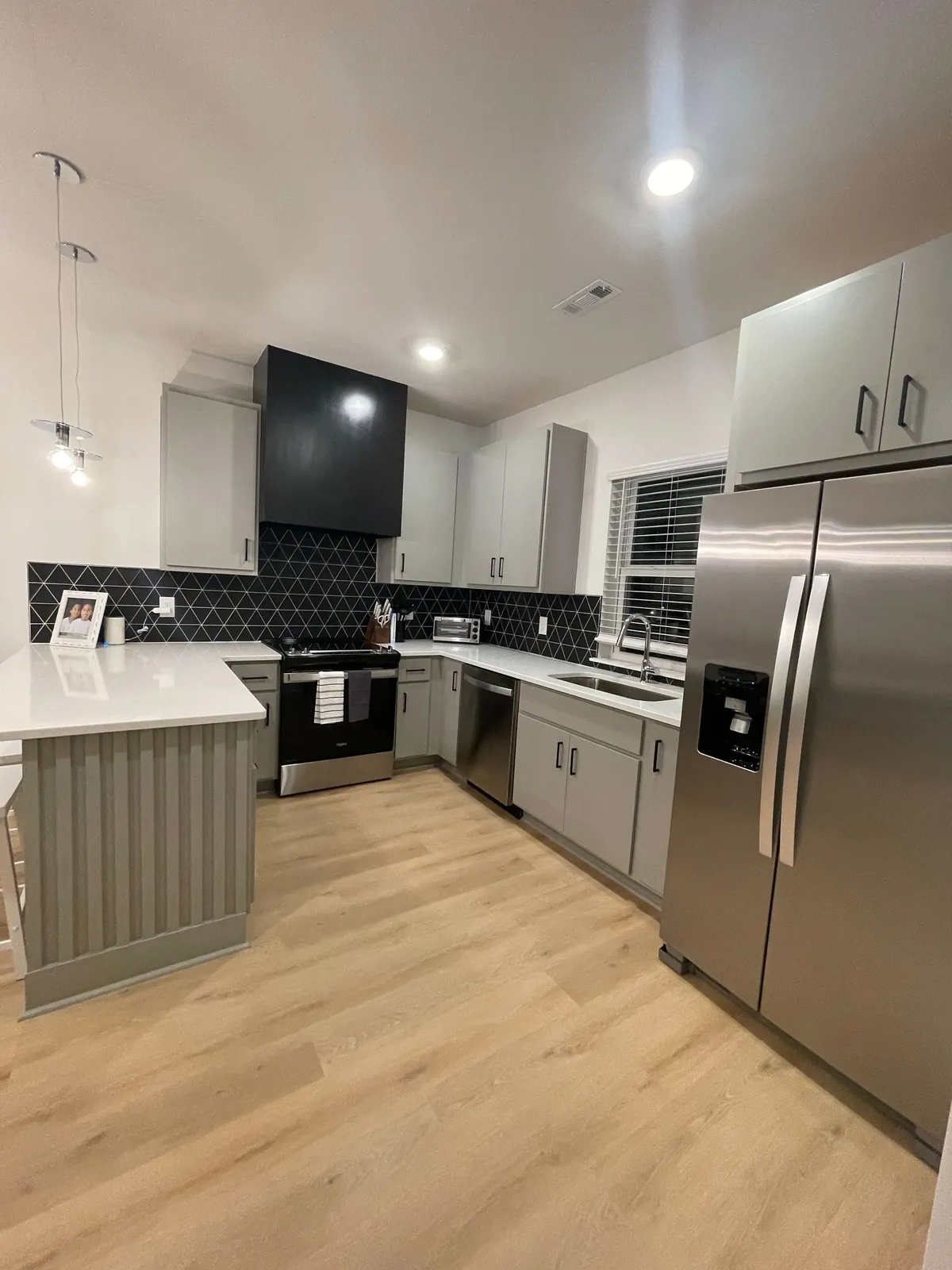 A bright, modern kitchen with sleek appliances, a large kitchen island ideal for meal prepping, and a geometric tile backsplash. The layout creates a welcoming space for cooking, entertaining, and gathering with friends or family.