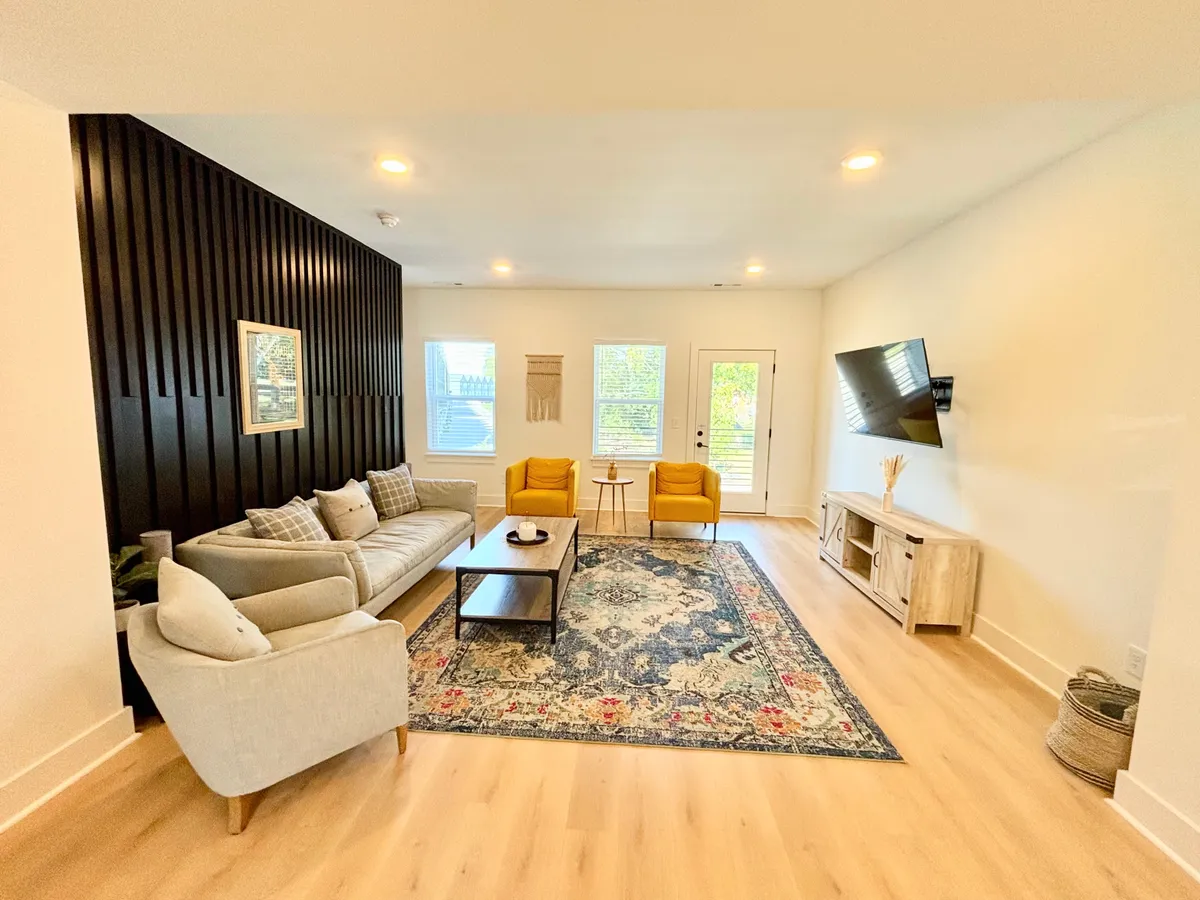 A cozy living room with a black accent wall, plush sofa, yellow chairs, a decorative rug, and a wall-mounted TV. The scene is inviting, suggesting a comfortable space for relaxation and entertainment.